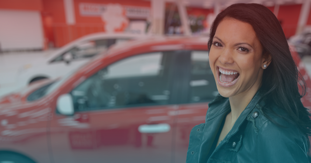 Mulher sorridente em primeiro plano à frente de diversos carros asiáticos em uma concessionária com tons de vermelho ao fundo.